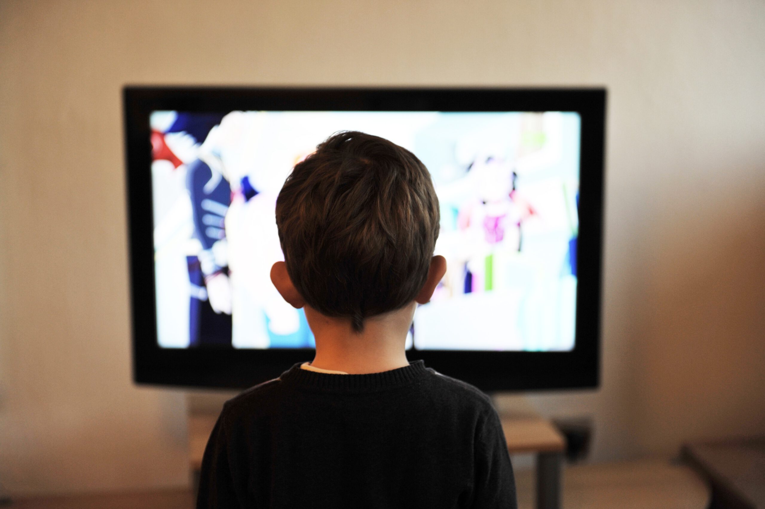 Im Vordergrund ist ein Kind zu sehen, welches auf einen Fernseher guckt, der im Hintergrund steht.