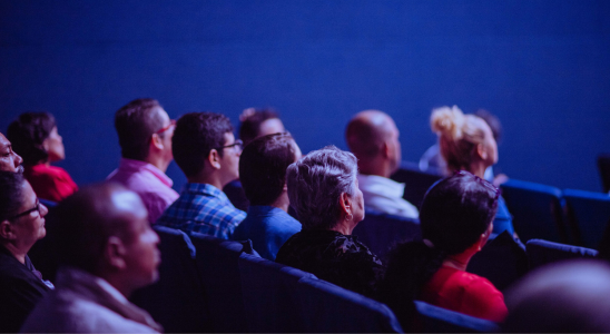 Menschen sitzen im Publikum vor dunkelblauen Hintergrund