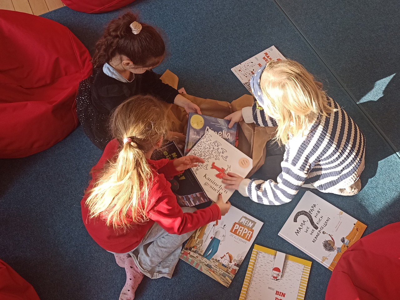 Drei Grundschulkinder sitzen auf dem Boden und beugen sich interessiert über Bilderbücher vom Schaltzeit Verlag.