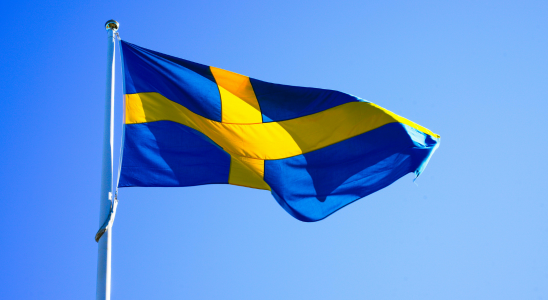 Schwedische Flagge an einer Fahnenstange weht im Wind. Im Hintergrund ist blauer Himmel zu sein.
