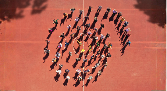 Gruppenfoto von oben, Menschen stehen auf einem Sportplatz, das Bild sieht aus wie eine Schlange