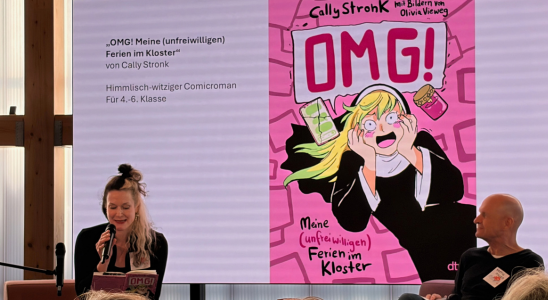 Cally Stronk sitzt vor einem großen Bildschirm. Darauf ist das Cover ihres Buches "OMG!" zu sehen.