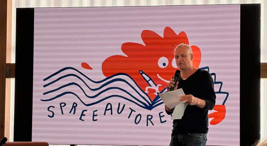 Martin Muser steht vor einem großen Bildschirm, auf dem das Spreeautoren-Logo zu sehen ist.